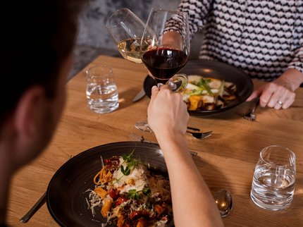 Alpine Kulinarik in Prutz Zwei Personen stoßen mit Weingläsern über einem gedeckten Tisch mit Essen an