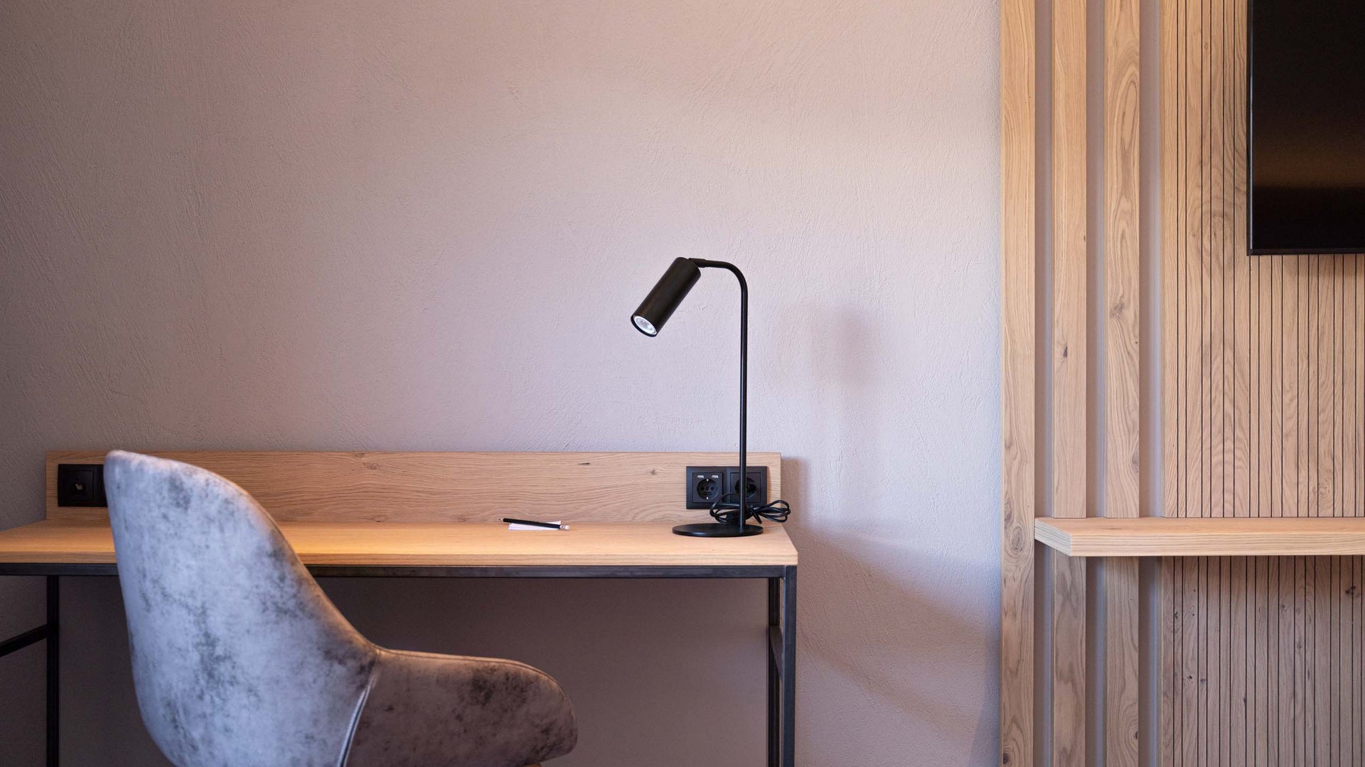 Feiern Sie Ihre Feste in Tirol Moderner Schreibtisch mit Lampe und grauem Stuhl vor weißer Wand