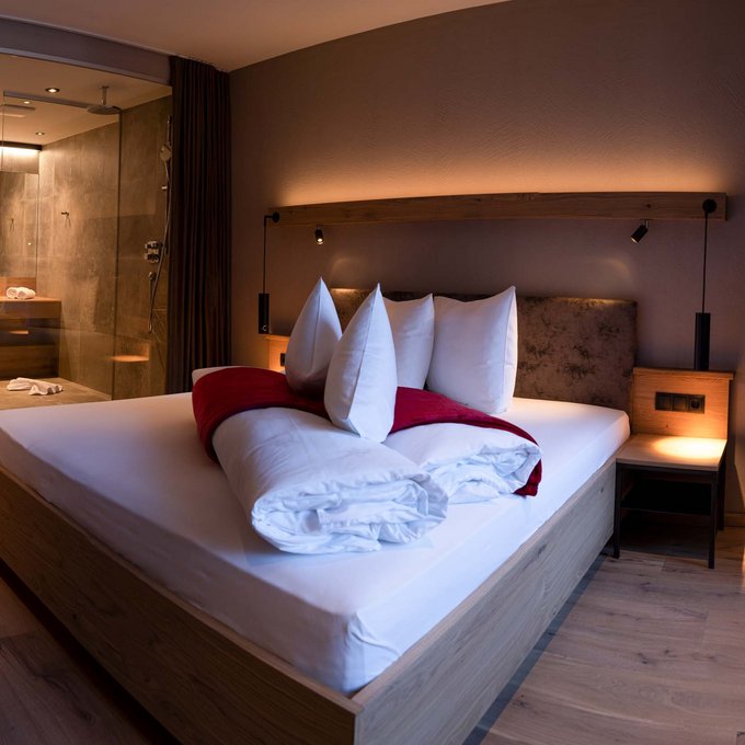 Hotel in Prutz gesucht? Modernes Schlafzimmer mit Holzboden, Bett und offener Dusche im Hintergrund
