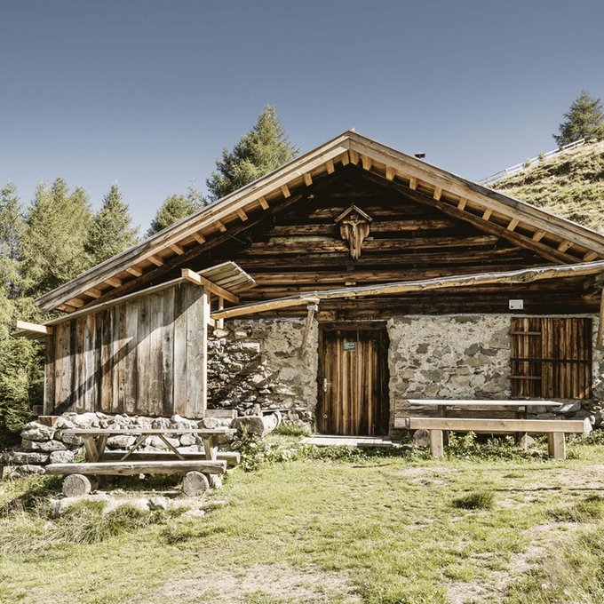 Entdecken Sie im Sommerurlaub die Tiroler Bergseen. Altes Holzhaus auf einer grünen Wiese umgeben von Bäumen und Hügeln