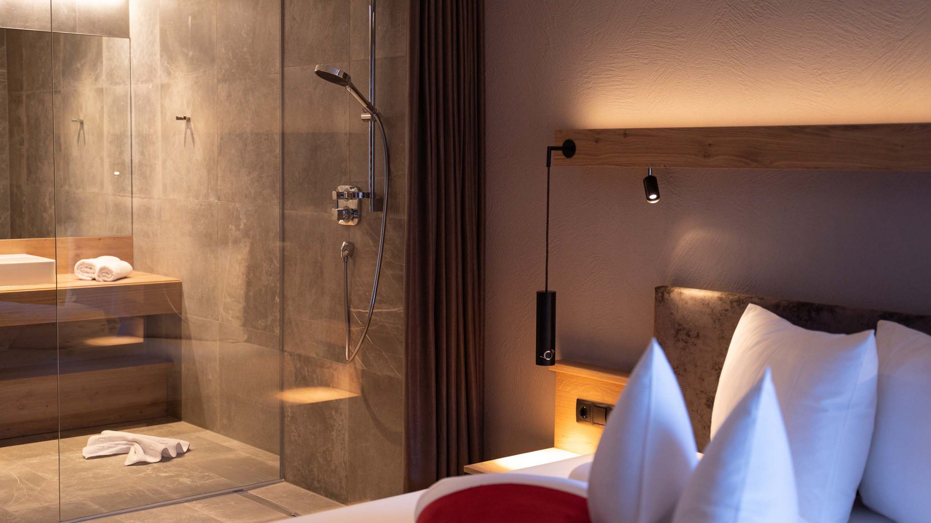 Feiern Sie Ihre Feste in Tirol Moderner Hotelzimmerbereich mit Dusche, Bett und stimmungsvoller Beleuchtung