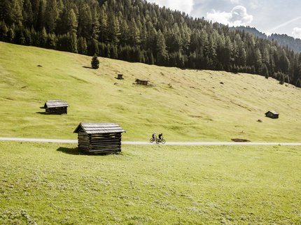 Hotel in Prutz gesucht? Zwei Radfahrer fahren auf einem Weg durch eine grüne Alm mit kleinen Hütten und Wäldern