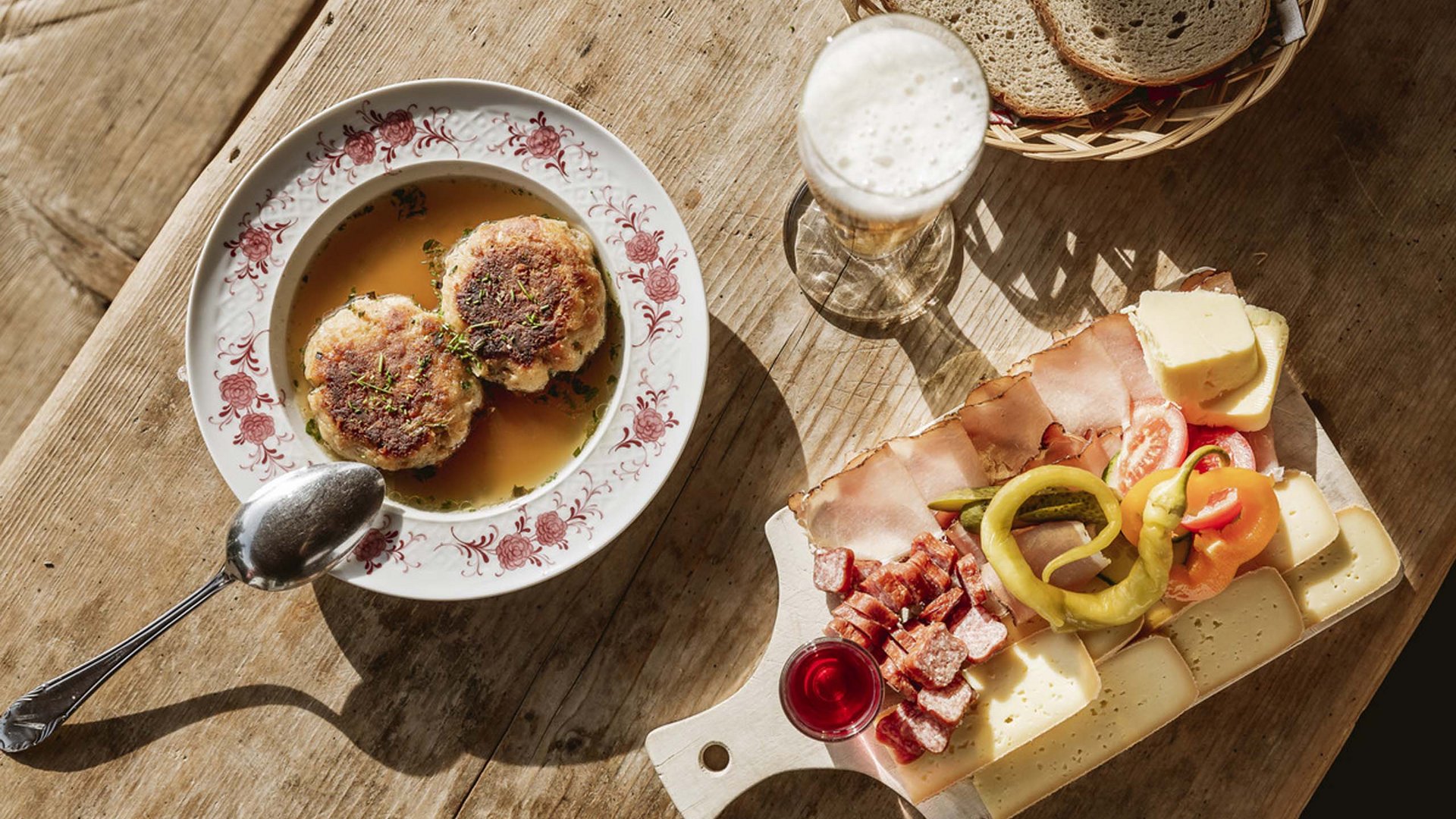 Entdecken Sie im Sommerurlaub die Tiroler Bergseen. Bayerisches Brotzeitbrettl mit Wurst, Käse, Senfgurke, Bier und Knödel in Brühe