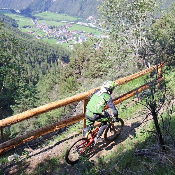 Ihr Radurlaub in Österreich/Tirol Mountainbiker auf Waldweg mit Blick auf Tal und Dorf in den Bergen