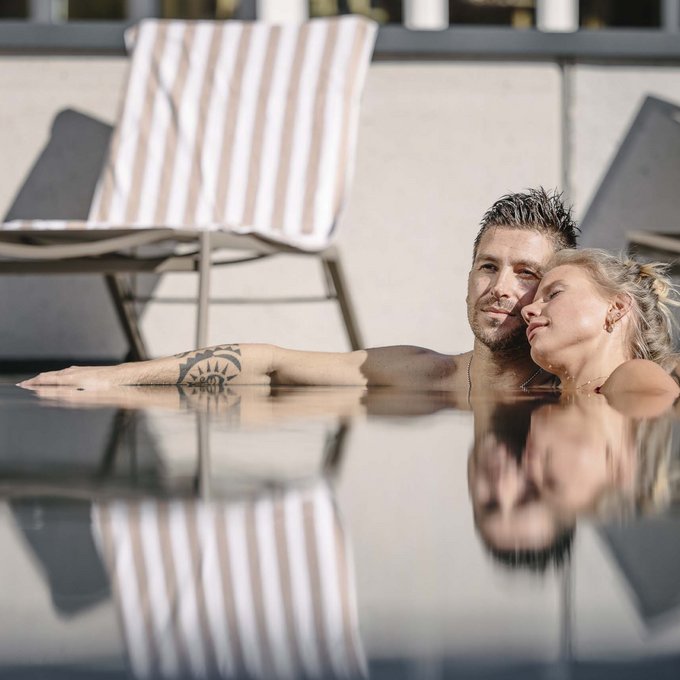 Outdoorpool Paar relaxt zusammen am Pool mit Liegestühlen und Handtuch im Hintergrund