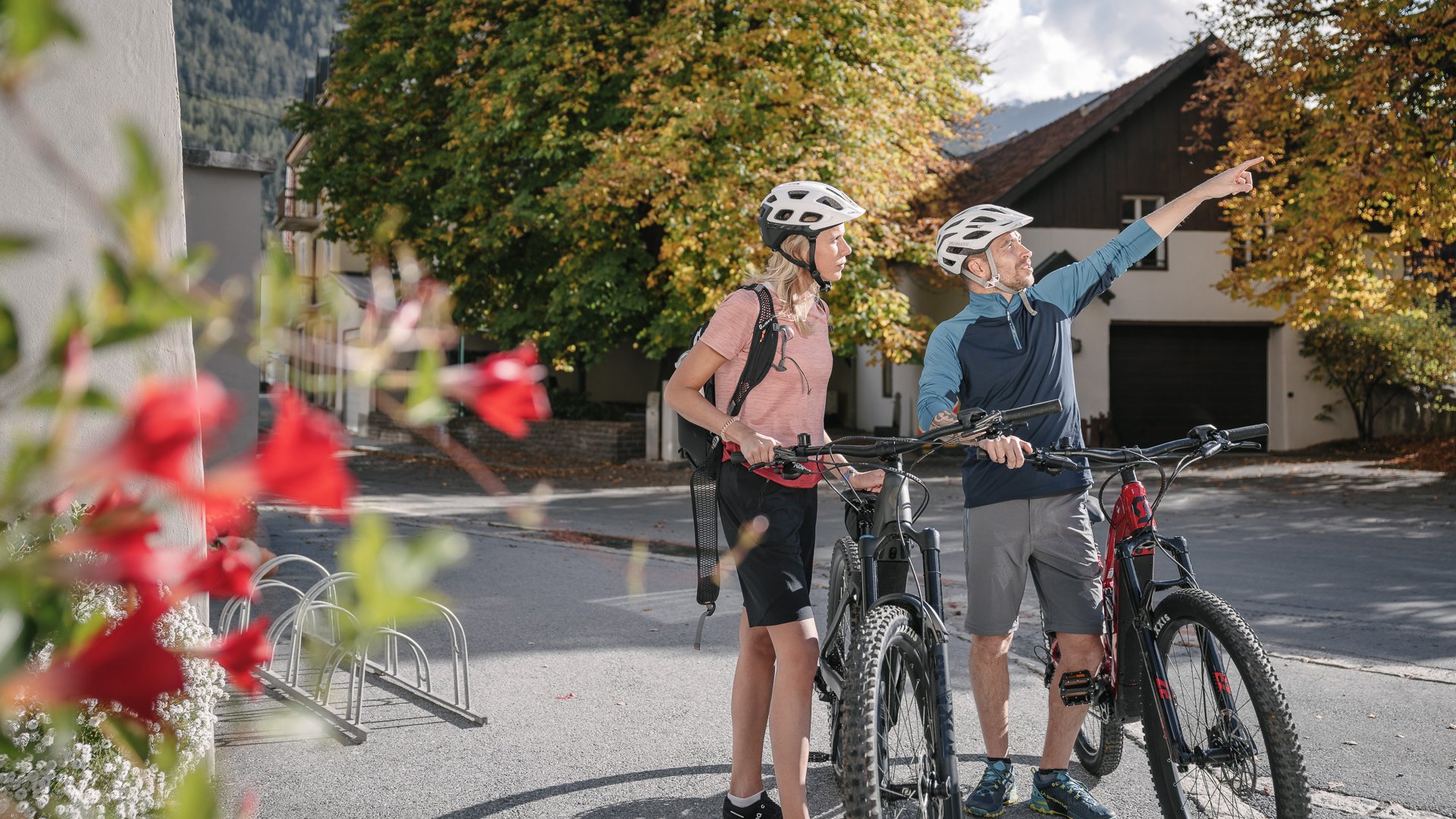 Entdecken Sie im Sommerurlaub die Tiroler Bergseen. Zwei Radfahrer stehen mit Helmen im Ort, ein Mann zeigt in die Ferne