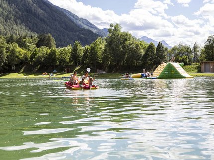 Entdecken Sie im Sommerurlaub die Tiroler Bergseen. Familie auf Tretboot auf See mit Hügeln und Wasserspielplatz im Hintergrund