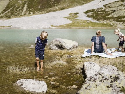 Entdecken Sie im Sommerurlaub die Tiroler Bergseen. Familie entspannt am Seeufer mit Kindern und Picknickdecke