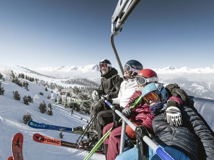 Winterurlaub in Tirol – Skispaß & Entspannung in den Alpen Vier Skifahrer auf einem Sessellift über verschneiter Berglandschaft