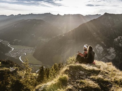 Hotel in Prutz gesucht? Zwei Wanderer sitzen auf Berggipfel mit Tal- und Flussblick bei Sonnenstrahlen