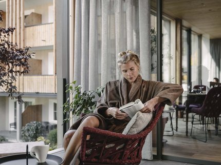 Wellnesshotel in Tirol gesucht? Frau liest entspannt Buch auf Balkon in Bademantel