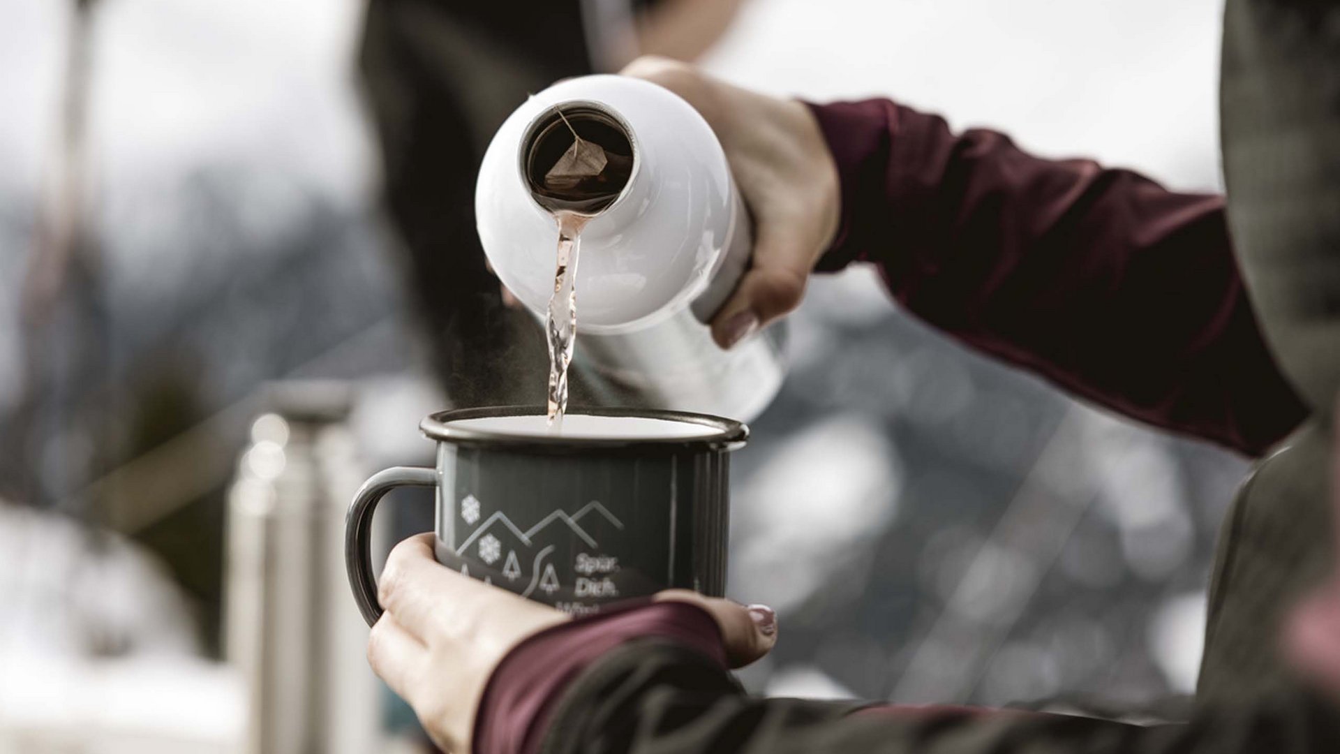 Skitouren Wasser wird aus einer Thermoskanne in eine Tasse im Freien gegossen