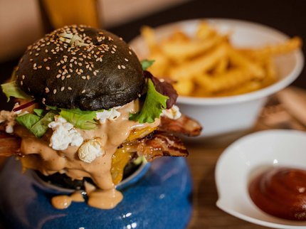 Alpine Kulinarik in Prutz Burger mit schwarzem Sesambrötchen, Käse, Speck, Salat und Soße mit Pommes und Ketchup