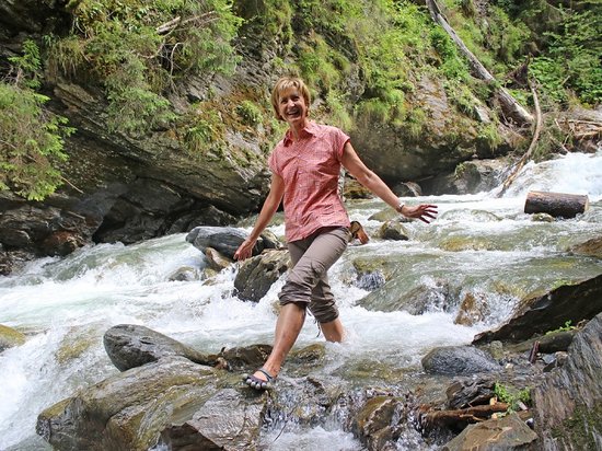 Echtes Kleinod aus dem Tiroler Oberland Frau balanciert lächelnd auf Steinen in einem Gebirgsbach im Wald