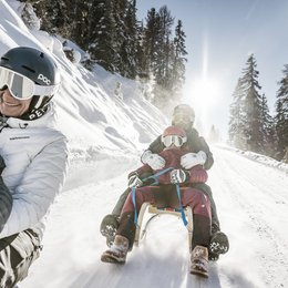 Ihr Wohlfühlort: das Hotel in Prutz im Tiroler Oberland ⛰️ Mehrere Personen genießen Schlittenfahrt auf schneebedecktem Bergweg bei sonnigem Wetter