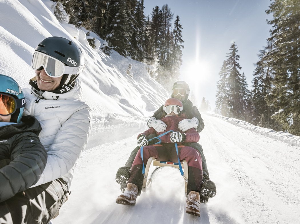 Winterspaß inmitten der Alpen Mehrere Personen genießen Schlittenfahrt auf schneebedecktem Bergweg bei sonnigem Wetter