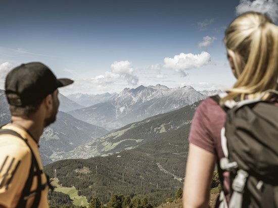 Echtes Kleinod aus dem Tiroler Oberland Zwei Wanderer mit Rucksäcken blicken auf eine Berglandschaft mit bewaldeten Hügeln