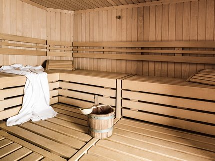 Wellnesshotel in Tirol gesucht? Leere Holzsauna mit Handtuch und Eimer mit Kelle auf dem Boden