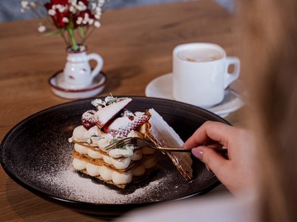Alpine Kulinarik in Prutz Person hält Gabel und isst Schichtdessert mit Puderzucker und Erdbeeren