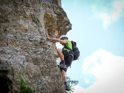 Entdecken Sie im Sommerurlaub die Tiroler Bergseen. Mann klettert mit Helm und Rucksack an Felswand im Freien