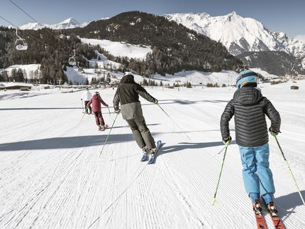 Hotel Post: Ihr Skihotel in Tirol Familie beim Skifahren auf präparierter Piste vor verschneiten Bergen