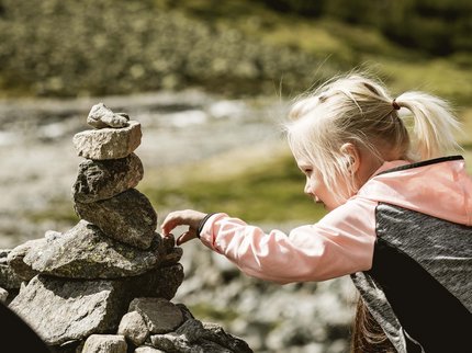 Entdecken Sie im Sommerurlaub die Tiroler Bergseen. Mädchen baut Steinmauer im Freien