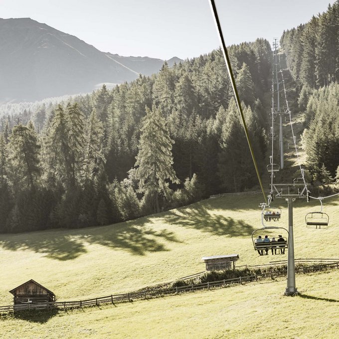 Entdecken Sie im Sommerurlaub die Tiroler Bergseen. Sessellift in sonniger Berglandschaft mit Wäldern und kleinen Holzhütten