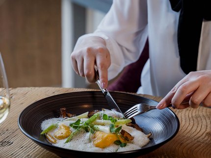 Alpine Kulinarik in Prutz Person isst ein Gericht mit Spargel, Pilzen und Schaum in einem schwarzen Teller