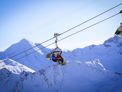 Hotel Post: Ihr Skihotel in Tirol Skifahrer in Sessellift über schneebedeckten Bergen bei klarem Himmel