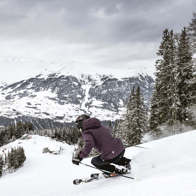 Winterurlaub in Tirol – Skispaß & Entspannung in den Alpen Skifahrer fährt eine verschneite Abfahrt mit Schnee und Bäumen im Hintergrund