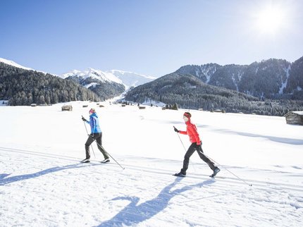 Winterurlaub in Tirol – Skispaß & Entspannung in den Alpen Zwei Personen beim Langlaufen in verschneiter Berglandschaft bei Sonnenschein