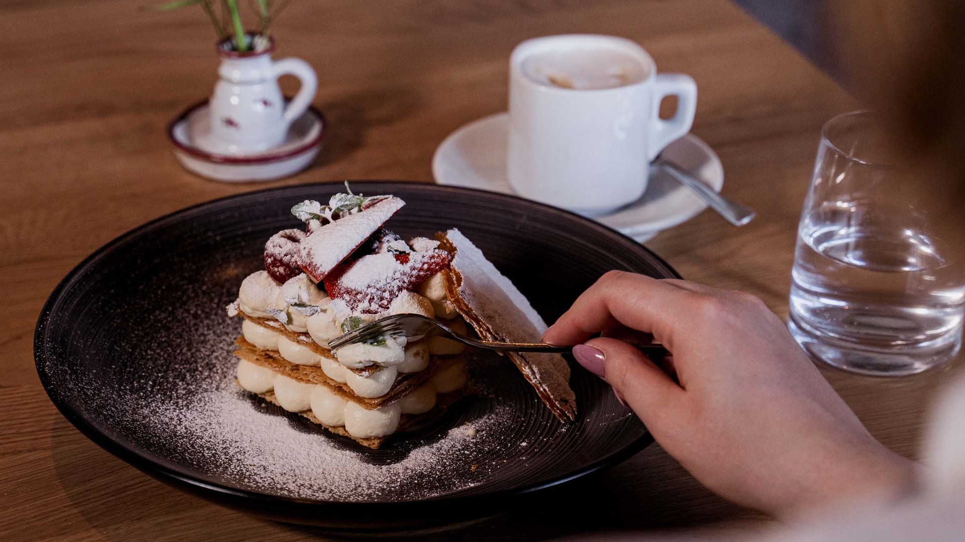 Alpine Kulinarik in Prutz Hand hält Gabel über Dessert mit Sahne und Erdbeeren auf schwarzem Teller