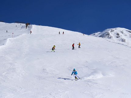 Hotel Post: Ihr Skihotel in Tirol Skifahrer fahren auf einer schneebedeckten Piste unter klarem blauem Himmel