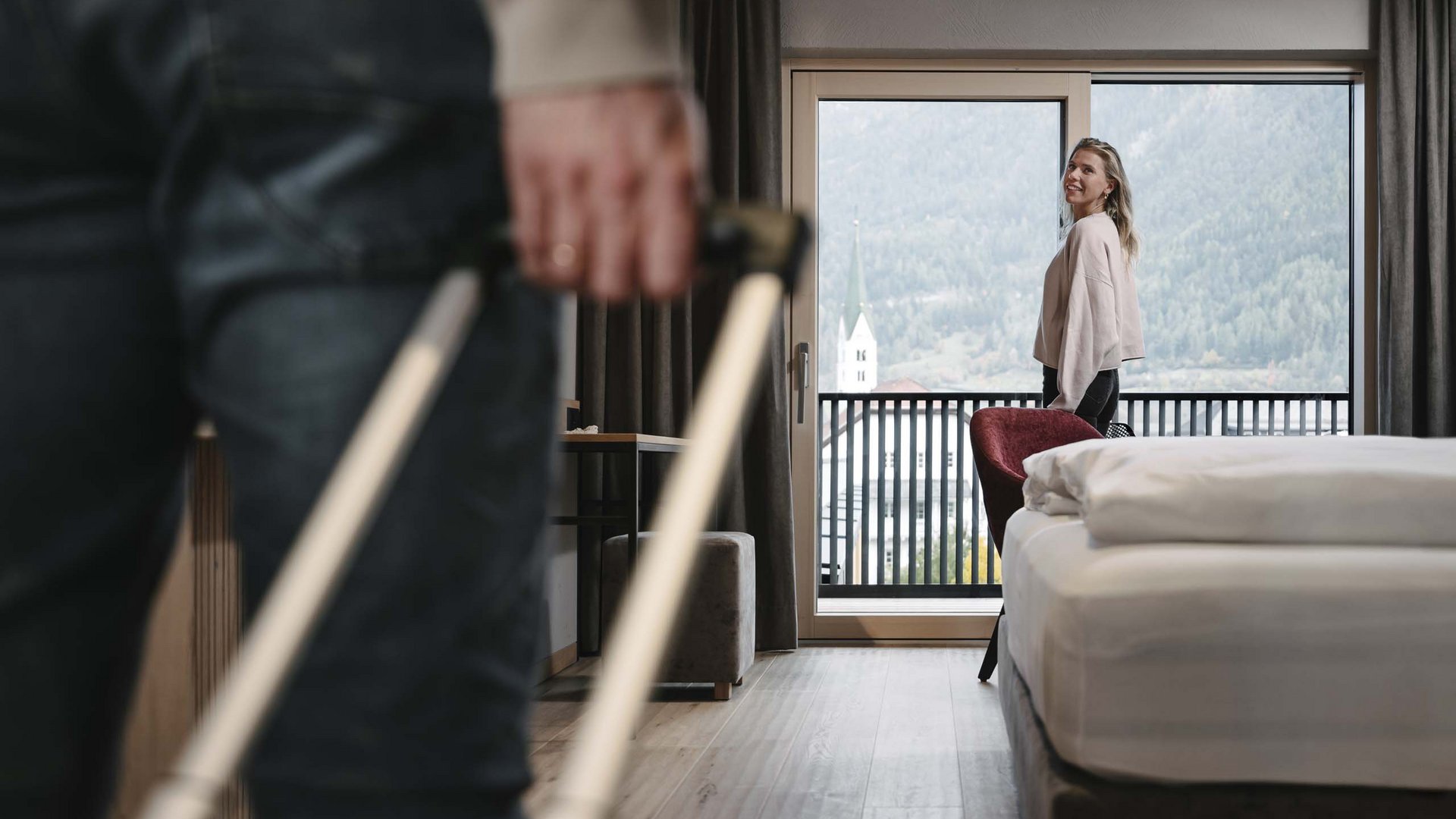 Hotel in Prutz gesucht? Person mit Koffer betritt Hotelzimmer, Frau blickt zum Fenster mit Bergblick