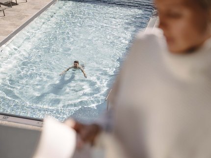 Ihr Urlaub im Sporthotel in Tirol Person schwimmt in klarem Pool, andere Person im Vordergrund unscharf