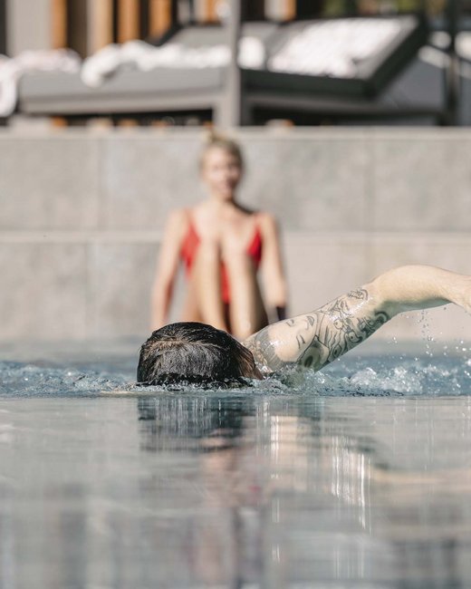 Ihr Wohlfühlort: das Hotel in Prutz im Tiroler Oberland ⛰️ Person schwimmt im Pool, andere sitzt in rotem Badeanzug am Beckenrand