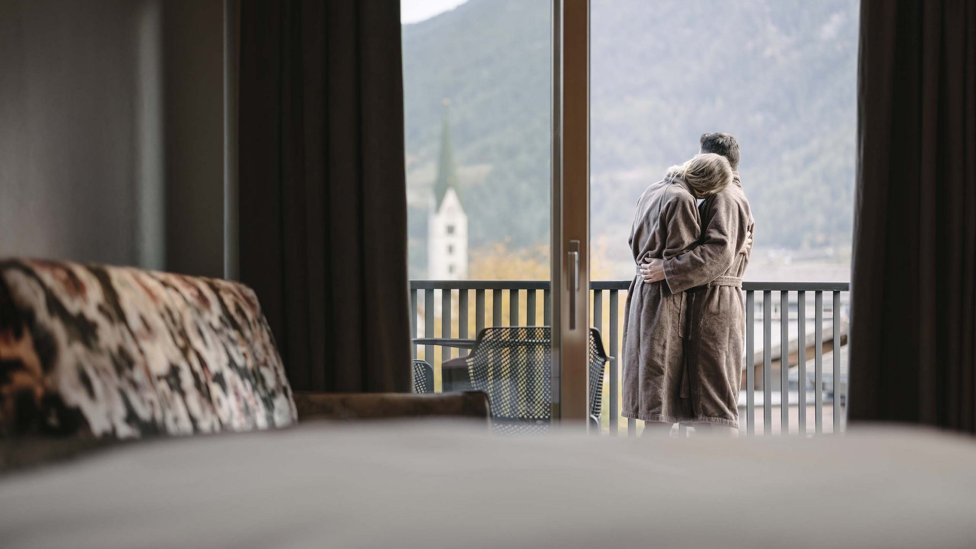 Ihr Wohlfühlort: das Hotel in Prutz im Tiroler Oberland ⛰️ Paar in Bademänteln umarmt sich auf Balkon mit Bergblick